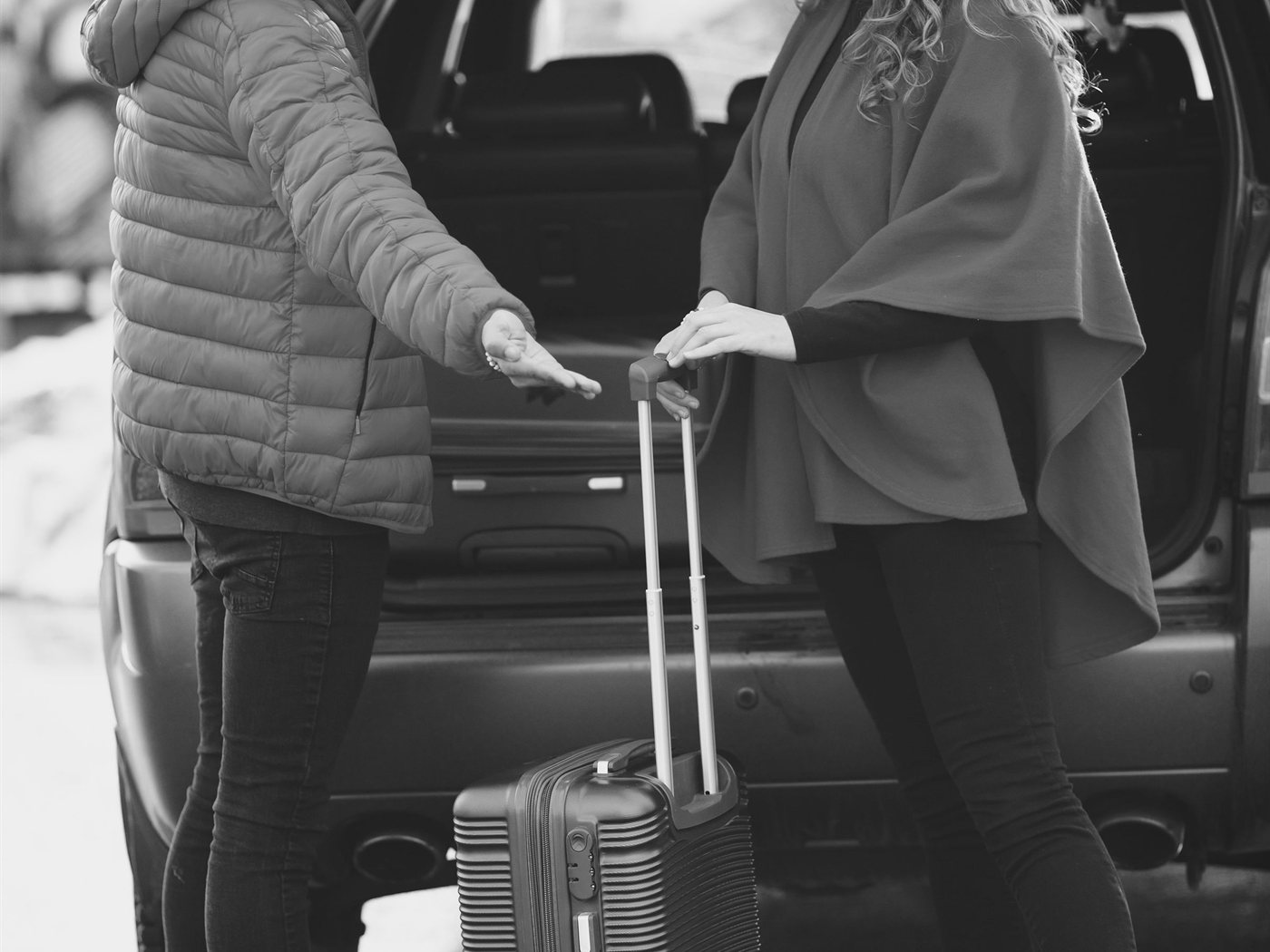 Two travellers with a suitcase at the open boot of a car